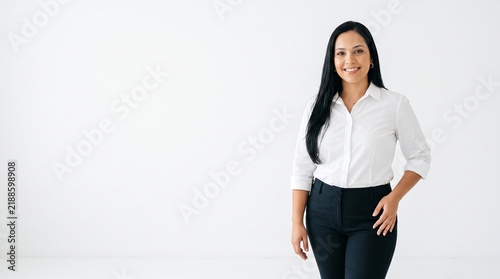 Confident professional woman in white shirt and black pants smiling against a clean white background