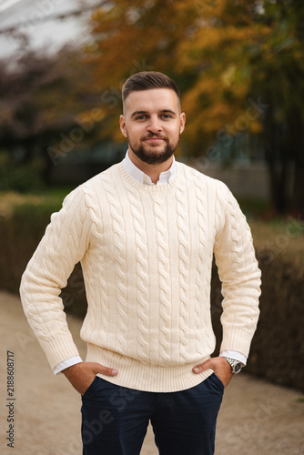 Taking a moment to relax outdoors, a casually dressed man sits comfortably in a stylish vest surrounded by autumn foliage. The cozy setting, natural light and warm colors create a calm seasonal atmosp