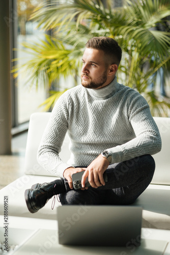 Business professional relaxing in a modern lounge area while talking on his phone. Professional lifestyle, relaxed atmosphere and natural light.