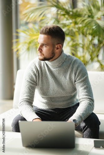 Business professional relaxing in a modern lounge area while talking on his phone. Professional lifestyle, relaxed atmosphere and natural light.