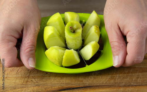 The person uses an apple slicer, pressing it through the center of the apple to cut it into sections and remove the core in home kitchen.