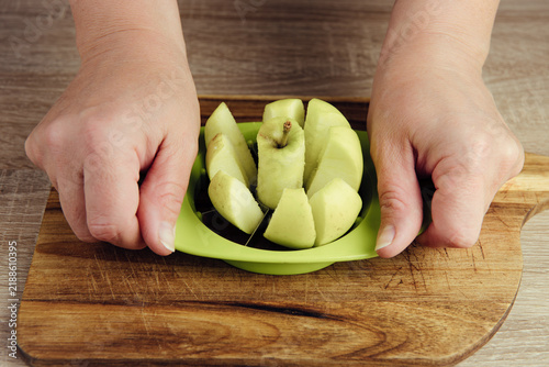 The person uses an apple slicer, pressing it through the center of the apple to cut it into sections and remove the core in home kitchen.