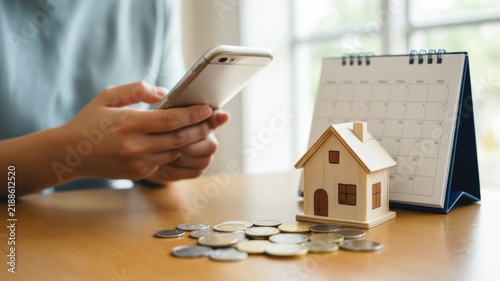 A Person Using A Smartphone Beside A Miniature House And Loose Coins