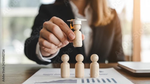 A Professional Placing A Graduation Cap On A Wooden Figurine Human Model