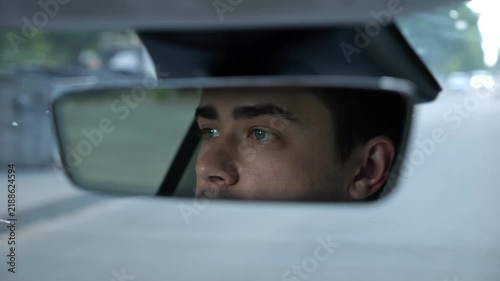 Male eyes of driver reflecting in rearview mirror while riding modern electric car. Young man looking concentrated to urban road during operating motor vehicle capturing focused gaze during city trip