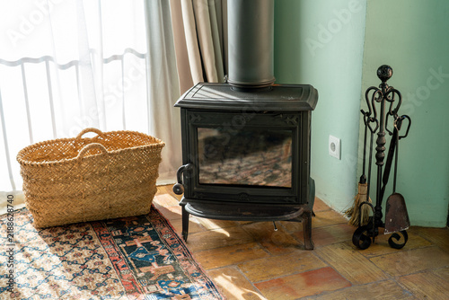 Cozy cottage interior with vintage cast iron wood burning stove. Authentic country house living room decoration, wicker basket, and rustic fireplace heating under soft natural light
