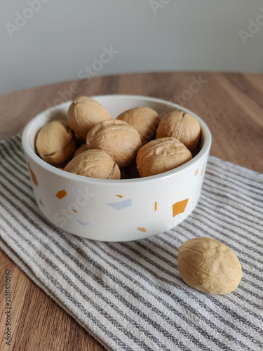 Whole walnuts in white ceramic bowl and striped kitchen cotton towel on wooden table.  Healthy eating, calories, diet, harvest. Shells of washed nuts are perfectly clean. Copy space. Close-up.