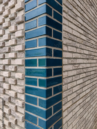 Corner of wall faced with light textured brick with vertical dark glazed brick inserts. Close-up