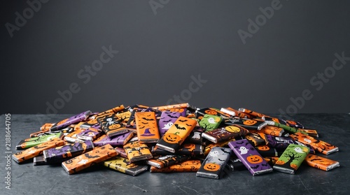 A large pile of individually wrapped Halloween chocolate bars with festive designs like pumpkins ghosts and bats