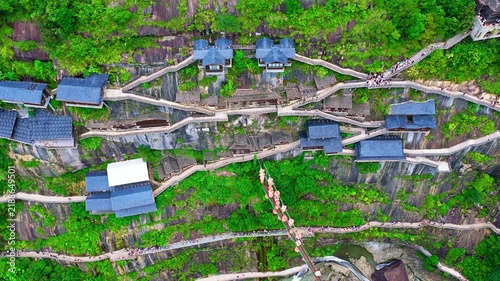 Aerial view of Wangxian Valley in Shangrao, Jiangxi, China, with winding stone stairways, blue-roofed pavilions, dense vegetation, and bright natural light.