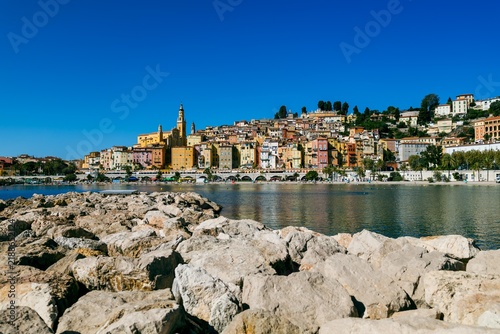 Colorful hillside buildings overlooking the beach and Mediterranean Sea in Menton, France, under a clear blue sky. French Riviera waterfront photographed in September 2026.