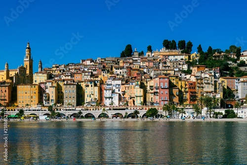 Colorful hillside buildings overlooking the beach and Mediterranean Sea in Menton, France, under a clear blue sky. French Riviera waterfront photographed in September 2026.