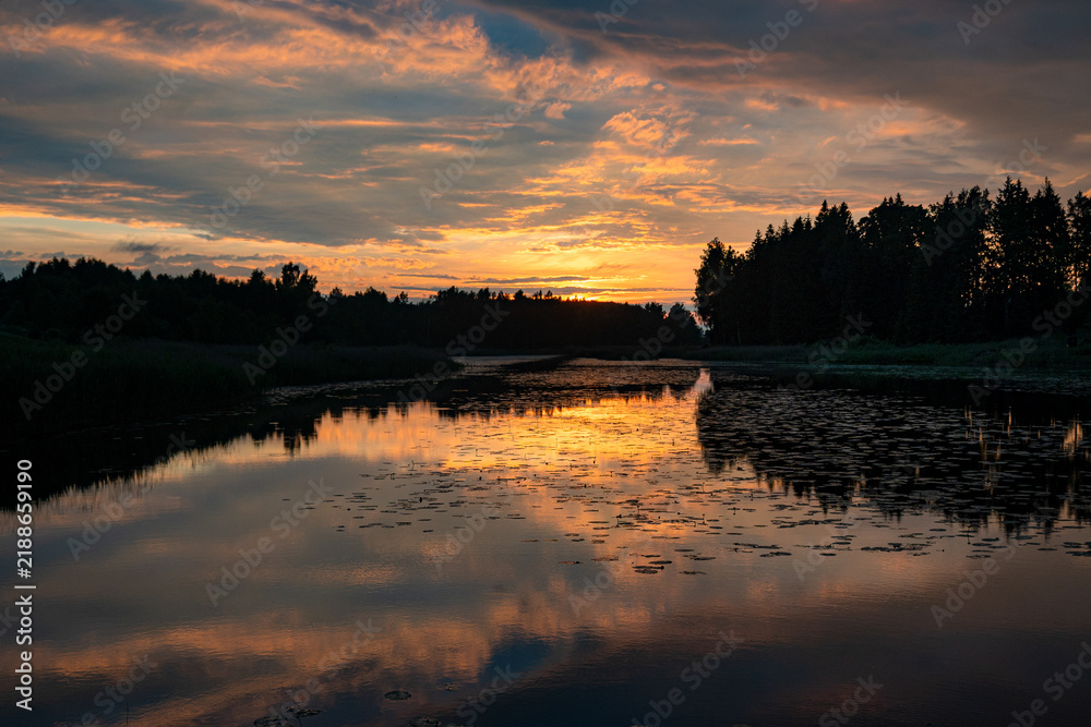 Obraz premium A magical landscape featuring a beautiful sunset or sunrise over a pond or lake on a summer evening, with a cloudy sky in the background, reflections on the water