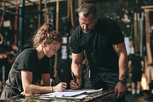 Fitness trainer helping a young woman write down workout notes inside a modern gym setting
