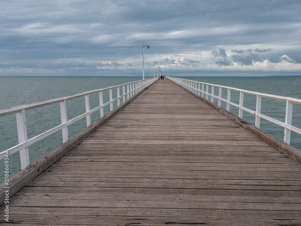 Fototapeta premium Long wooden pier with white railings extending into calm ocean in Australia