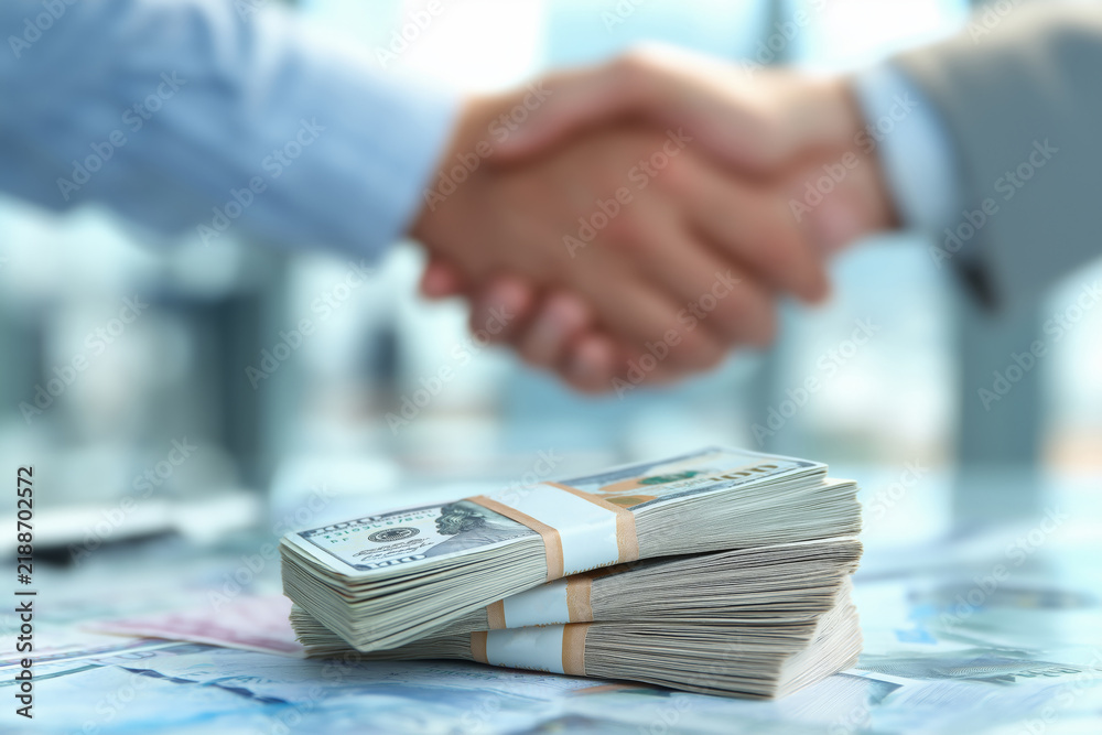 Obraz premium Business handshake over a blurred cash background, representing financial agreement, partnership, investment deal, corporate finance collaboration, and trust in monetary or banking transactions.