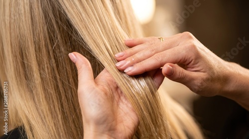 Hairdresser applying treatment to blonde hair, close-up on hands and hair strands