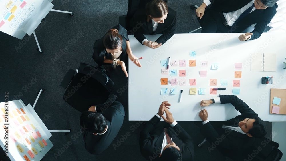 Obraz premium Top view of investor writing white board to present project and putting hand together with professional business team to celebrate successful project at meeting table with sticky note. Directorate.