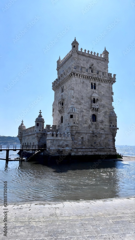 Fototapeta premium Belem Tower reflecting in the calm waters of the Tagus River under a clear blue sky, Lisbon, Portugal