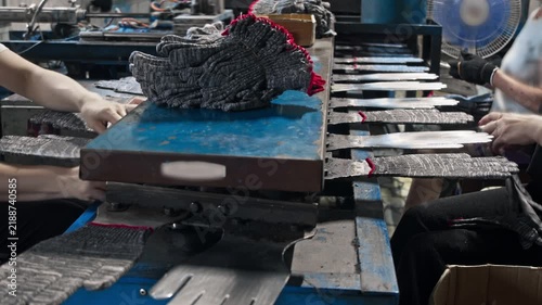 Close up shot reveals textile factory workers placing knitted grey work gloves onto metal shaping molds. Industrial manufacturing line processes protective hand wear during busy production shift.