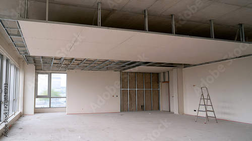 Commercial office interior space under construction with metal frame false ceiling structure drywall partitions and step ladder in empty room
