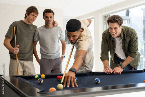 Diverse male friends playing billiards in rec room, shooter aiming cue with scattered balls