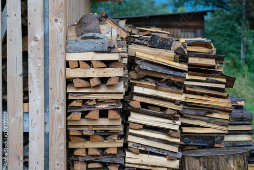 Large woodpile of chopped firewood logs stored in a rural backyard. Authentic winterization concept, domestic biomass heating supply, and rustic timber texture background.