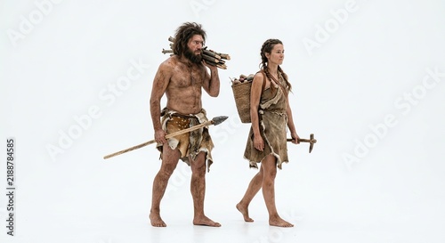 Full-length studio shot of prehistoric caveman carrying firewood and a woman carrying a wicker basket walking isolated on a white background.