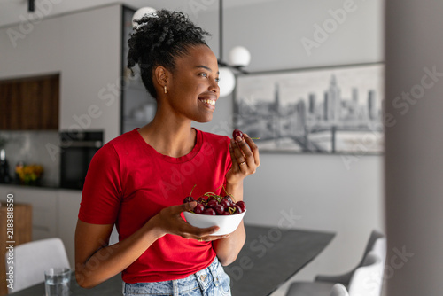 Smiling woman holding bowl of cherries in modern kitchen enjoying a healthy snack