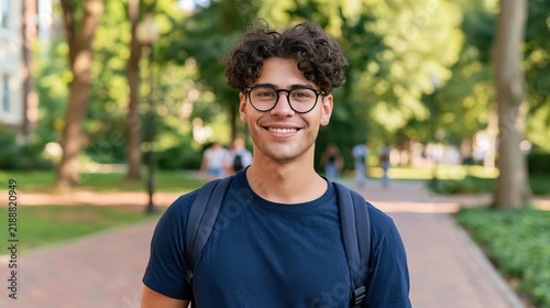 Smiling young man with curly hair and glasses on a college campus