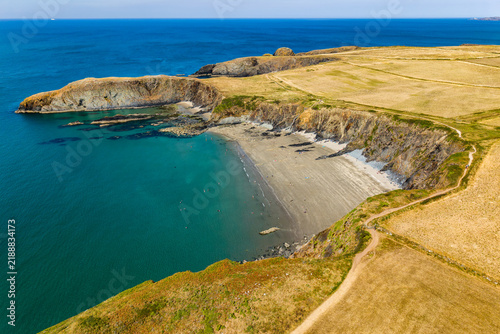 Картината върху платно Turquoise waters lapping sandy beach framed by rugged cliffs and dry summer fiel
