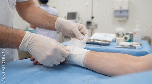 Healthcare professional meticulously applying a sterile dressing to a patient's arm, providing essential medical care and wound treatment in a clinical environment