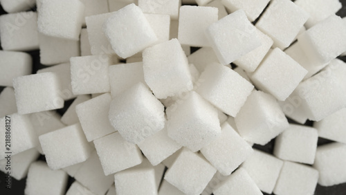 White sugar cubes piled together in an overhead close-up, scattered across a dark surface with visible crystalline texture.