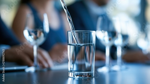 Pouring Clear Water into a Glass on a Table with People in the Background