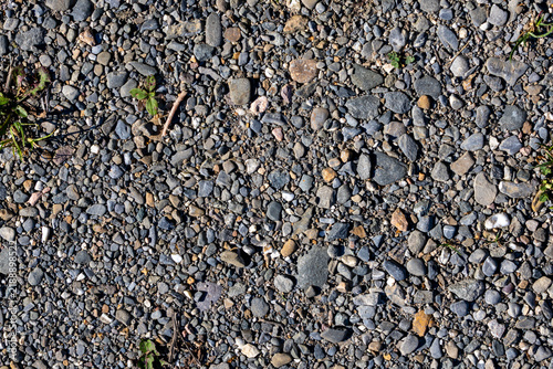 Quebec, Canada, 22 August 2026 : Full frame top down view of textured gravel ground surface with small stones and sparse vegetation