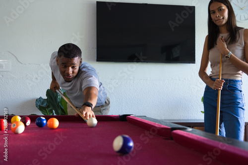 African American couple playing pool at home, man leaning over burgundy pool table aiming cue