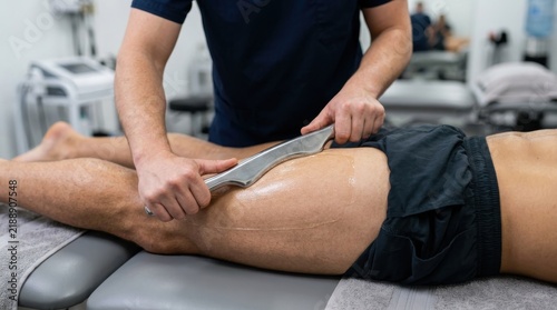 Physiotherapist performing Graston technique or soft tissue mobilization on a male patient's leg in a clinic