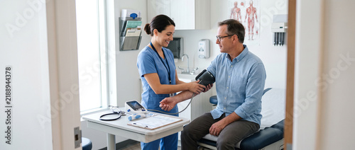 Medical assistant prepares adult patient for routine examination, checking blood pressure and vital signs to support primary care, preventive medicine, outpatient services and clinical workflow.