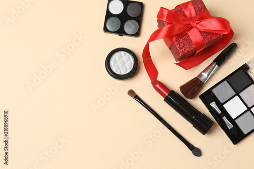 Cosmetics and brushes on a beige background, along with a gift box; beauty and skincare products.
