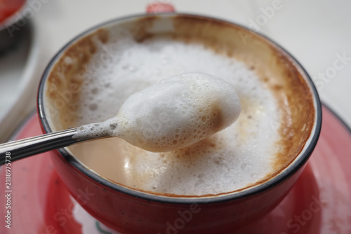 A steaming cup of coffee topped with frothy foam sits elegantly on a table, nestled within a vibrant red cup