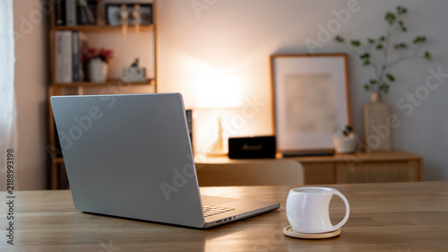 Laptop back view on wooden table with white coffee cup in warm cozy home office