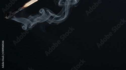 Smoke wisps rising from extinguished match on black background.