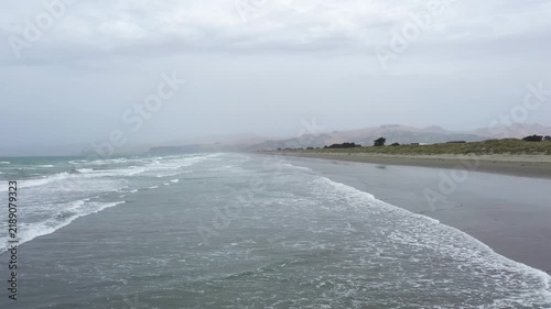 Aerial view of misty coastline with crashing ocean waves on sandy beach.
