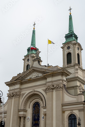 Vertical photo of a catholic church in Poland with a Polish and a Vatican city flags hanging from poles waving in the sky.