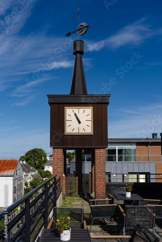 Bild auf Leinwand Modern clock tower on rooftop terrace with outdoor furniture under blue sky