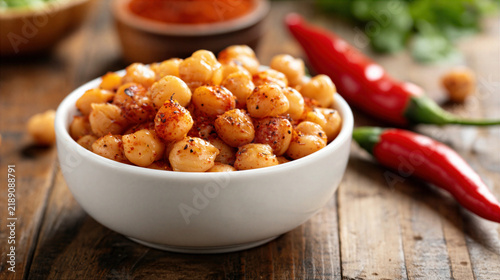 Roasted chickpea snack with chili pepper and spices in white bowl on wooden table