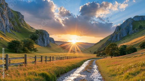 Scenic country road winding through a mountain valley at sunset, surrounded by golden fields, wildflowers, wooden fences, and dramatic peaks.