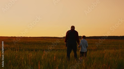 Grandfather and child walking hand in hand through peaceful countryside field at golden sunset, sharing quiet moments of bonding, reflection, and togetherness