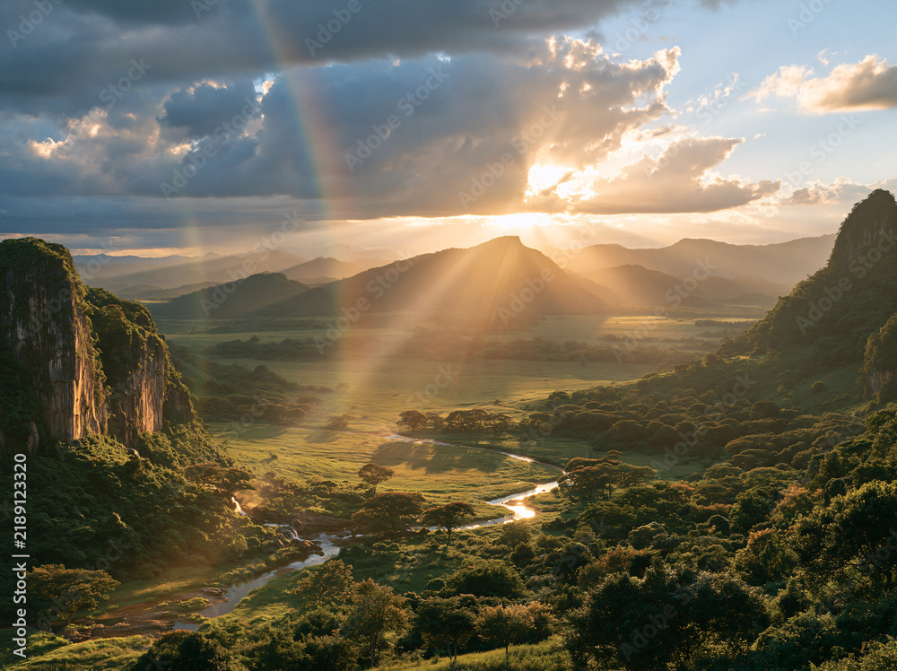 Obraz premium Golden sunset spills over mountain valley lake, twin rainbows arch above green woodland, tiny hikers stand on grassy meadow.