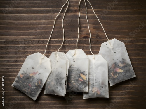 Five used tea bags hanging on wooden surface with visible loose leaves and specks